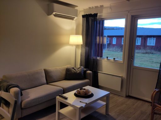 Ljust och luftigt vardagsrum med soffa, lampa och dörr till uteplats.