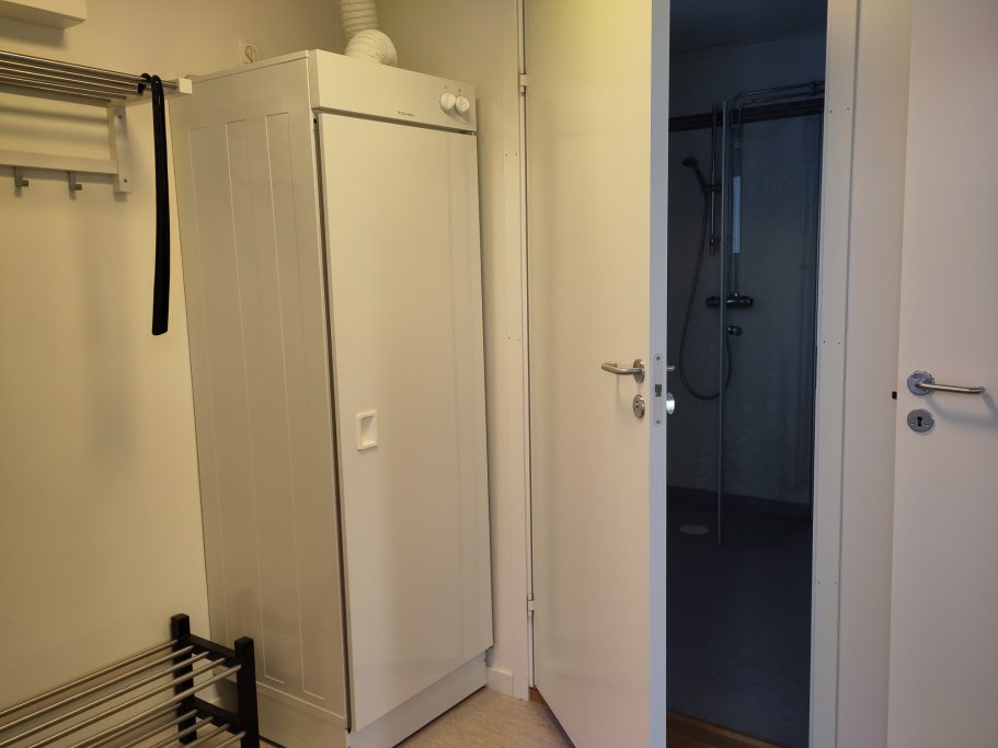 Hall Vitt skåp bredvid en öppen dörr som leder till ett rum.