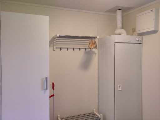 Vitt skåp med hyllor och frys på en ljus vägg i ett rum.