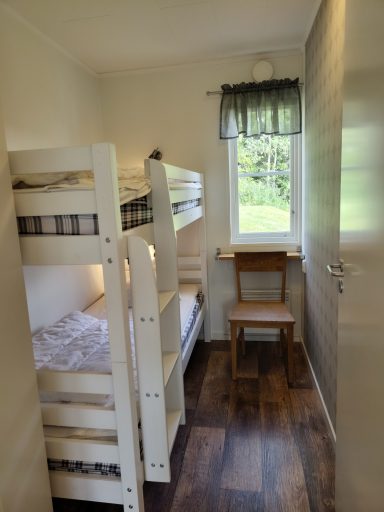 Rum med våningssäng, fönster med utsikt och en stol vid väggen.