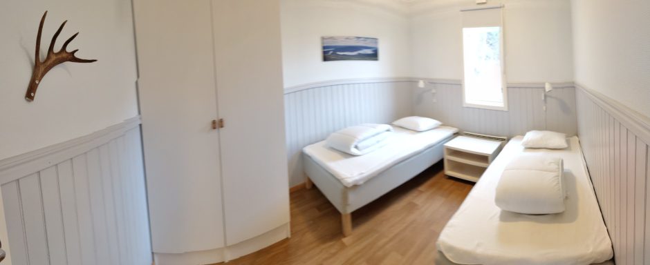 Två sängar i ett ljust rum med vita väggar och en liten fönster. En väggdekoration av horn.