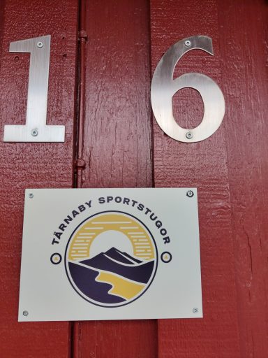 Nummer 16 med en logotyp av en sol och berg, placerad på en röd vägg.