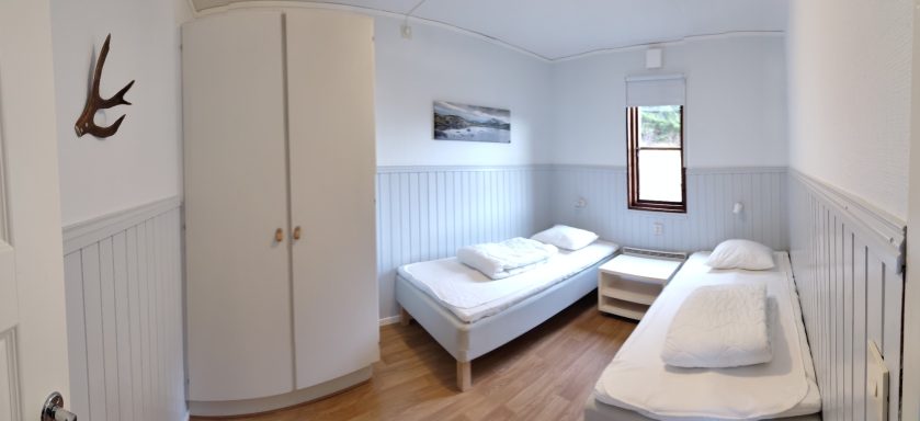 Ljust rum med två enkelsängar, garderob och fönster.