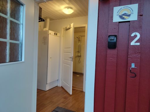 Ingång till en ljus hall med vit dörr och röd vägg på vänster sida.