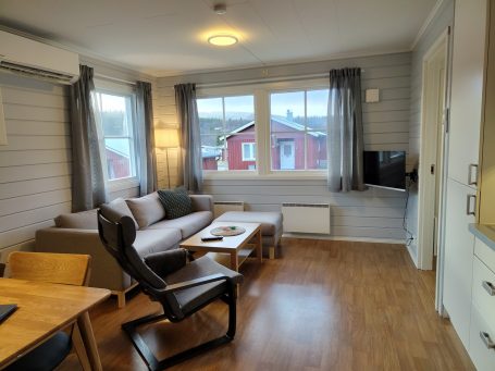 Ljust och modernt rum med soffa, bord och TV, fönster mot utsidan.