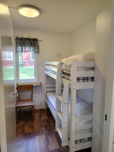 Rum med våningssängar, fönster, stol och trägolv.