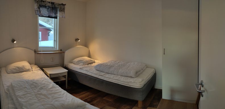 Två sängar i ett ljust rum med fönster och en dörr.