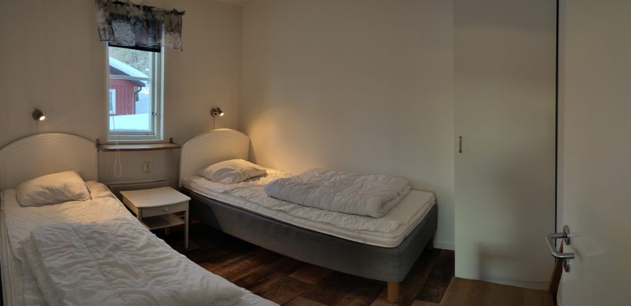 Sovrum 1 Två sängar i ett ljust rum med fönster och en dörr.