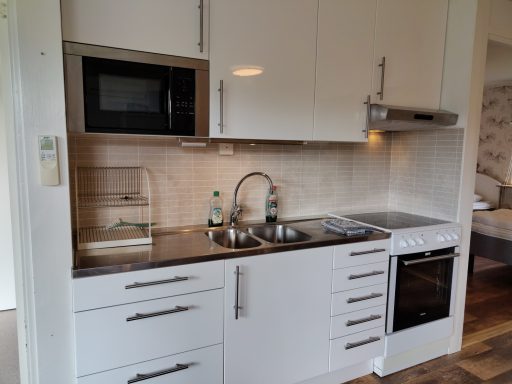 Kök med vit inredning, mikrovågsugn, spis och diskho.