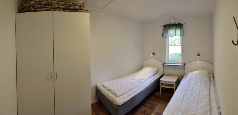 Litet rum med två enkelsängar, garderob och fönster med utsikt.