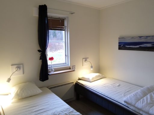 Två enkelsängar med lampor i ett ljust rum med fönster och målning på väggen.