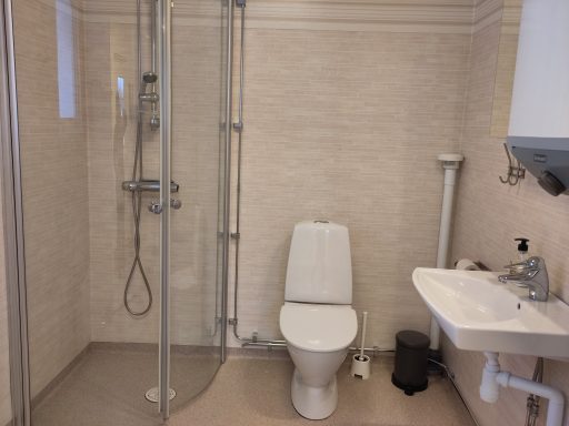 Badrum med dusch, toalett och handfat på beige väggar.