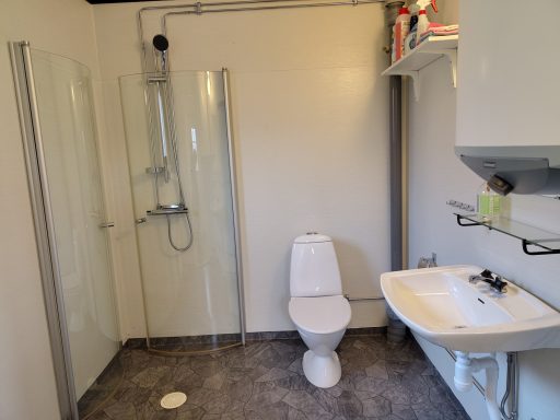 Badrum med dusch, toalett och handfat, ljusa väggar och grått golv.