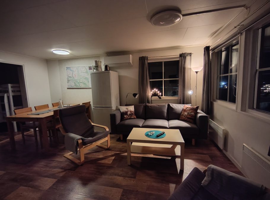 Vardagsrum och matplats Vardagsrum med en soffa, stolar, bord och fönster som släpper in mörkt ljus.