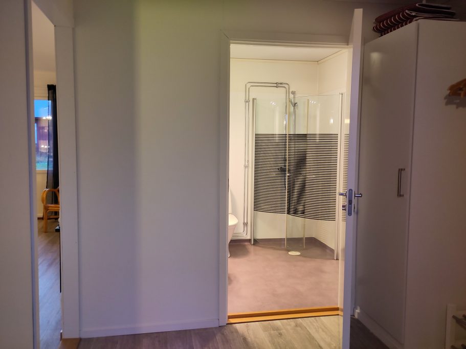 Hall, badrum, allrum En dörröppning som leder till ett badrum med dusch och grått mattgolv.
