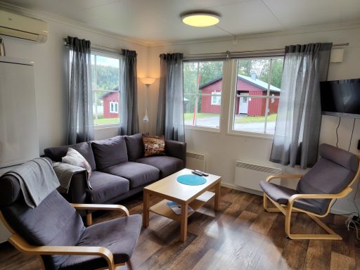 Inbjudande stuga med enmysig sittgrupp, fönster med utsikt mot röda hus.