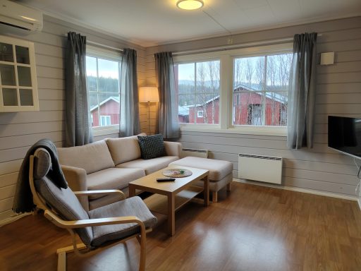 Vardagsrum med soffa, fåtölj och fönster som vetter mot röda stugor utanför.