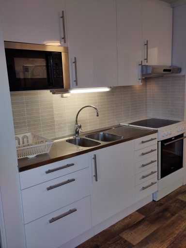 Modernt kök med vit inredning, dubbel diskho och spis med ugn.