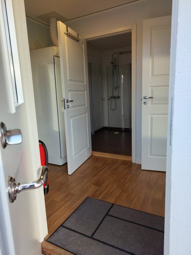 En öppen dörr med en genomgång till ett ljust rum och ett badrum i bakgrunden.