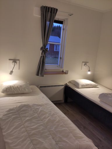 Två enkelsängar i ett rum med gardiner och vägglampor.