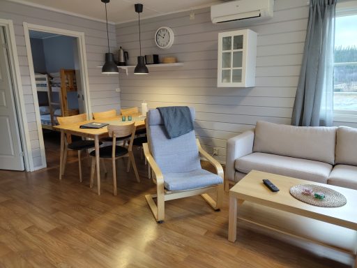 Ljust och luftigt vardagsrum med soffa, fåtölj, matbord och naturligt ljus.