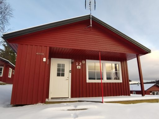 Röd stuga med snötäckta marker och fönster, belägen i en lugn miljö.