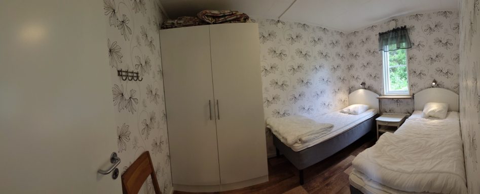 Sovrum med två sängar, vit garderob och blommigt tapet.