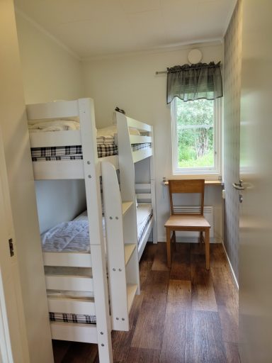 Sovrum med våningssäng, stol och fönster som vetter mot grönska utanför.