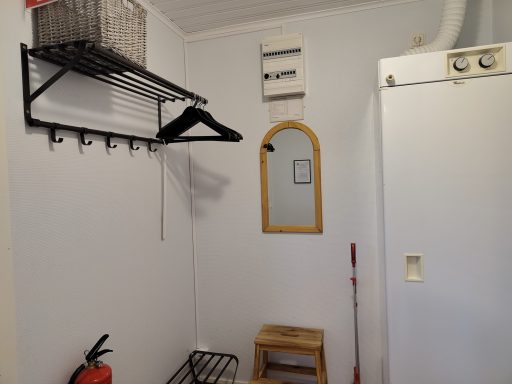 Vitt rum med en spegel, klädhängare och förvaringshylla.