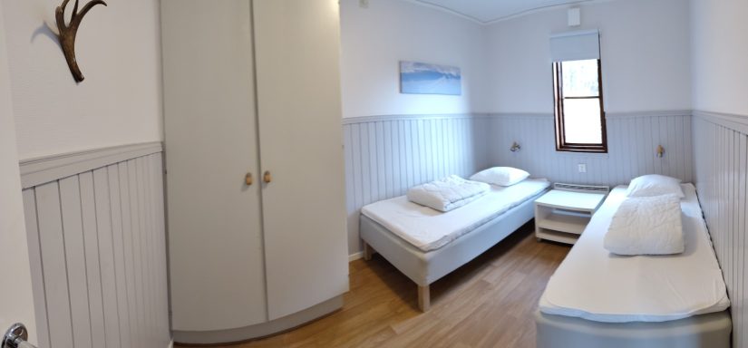 Ett ljust rum med två enkelsängar och en garderob.