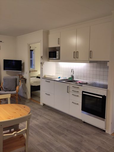 Ljust kök med vit inredning, ugn, mikrovågsugn och en matplats i hörnet.