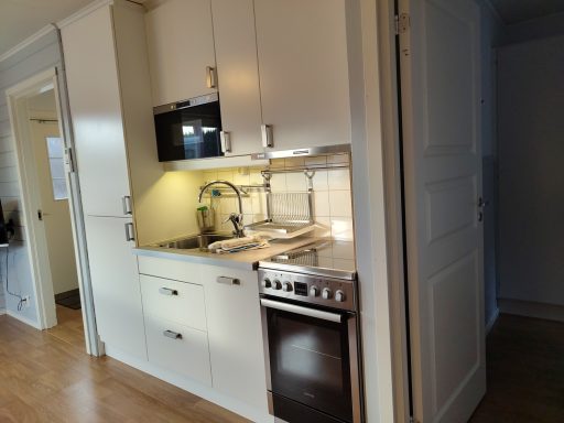 Kök med vit inredning, rostfri diskho och modern köksutrustning.