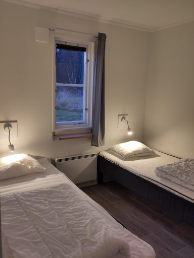 Två sängar i ett ljust rum med fönster och nattlampor.