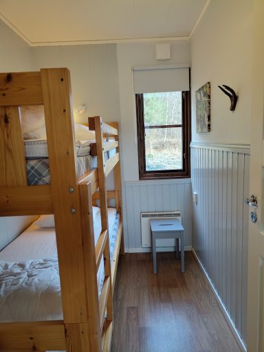 Litet rum med våningssäng, fönster och en stol i trä.