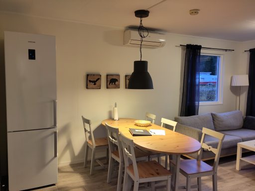 Kök med ett matbord, stolar, kylskåp och soffa i en ljus miljö.