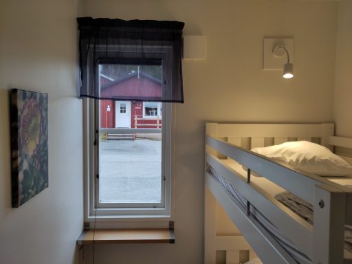 Sovrum med loftsäng, fönster mot en gård med röda hus.