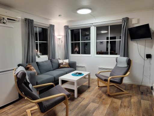 Modernt vardagsrum med soffa, stolar, ett litet bord och stora fönster.