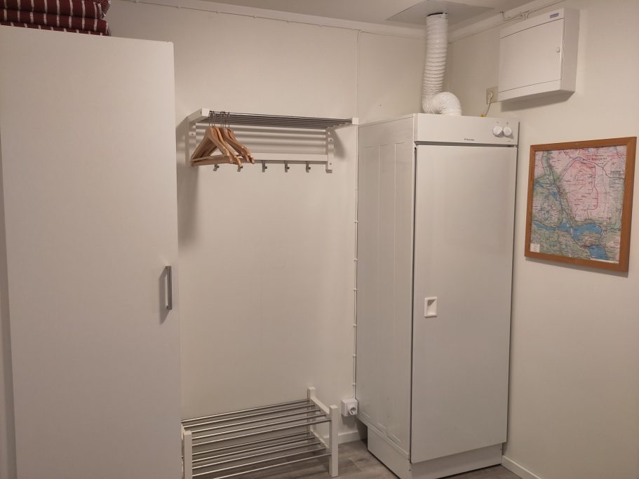 Hall Vitt rum med klädställning, frys och en karta på väggen.