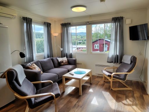 Modernt vardagsrum med soffa, fåtöljer och stora fönster som ger utsikt över landskapet.