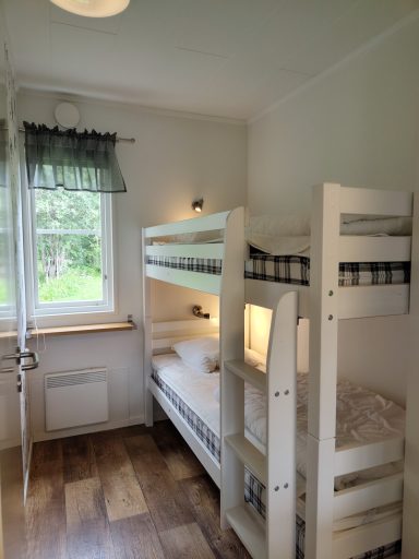 Sovrum med våningssäng och fönster som ger naturligt ljus. Trägolv och ljusa väggar.