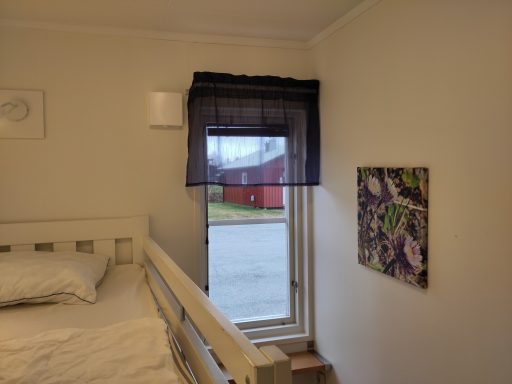 Inre i ett rum med säng, fönster med mörkläggningsgardin och väggkonst.