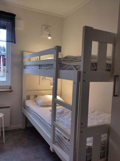 Sovrum med våningssäng och en stol, ljusväggar och mjukt golv.