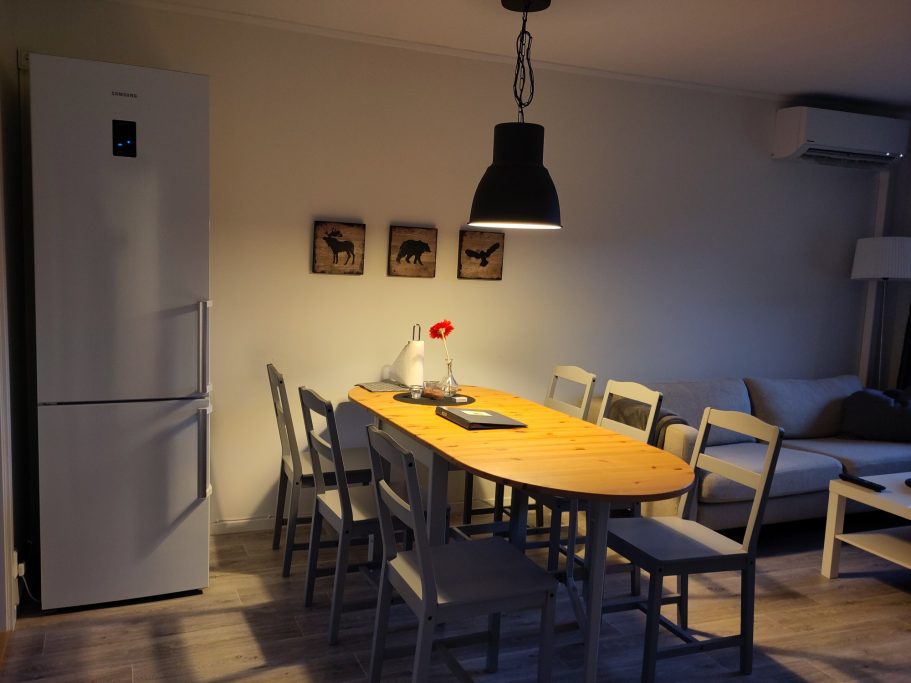 Matplats, kyl/frys Kök med ett stort bord, stolar, kylskåp, och en lampa hängande ovanför.