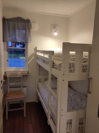 Litet rum med våningssäng, stol och fönster med gardin.