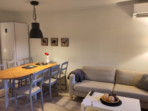 Ljust kök med matbord, stolar, soffa och detaljer på väggen.