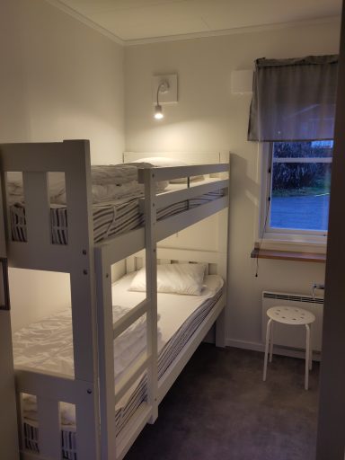 Sovrum med våningssäng, stol och fönster med gardin. Mjukt ljus skapar en lugn atmosfär.