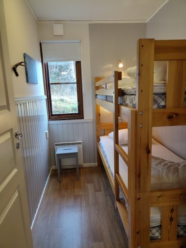 Litet rum med våningssäng, stol och fönster som släpper in dagsljus.