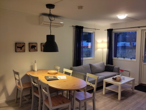 Ljust vardagsrum med soffgrupp, matbord och fönster mot utomhus.