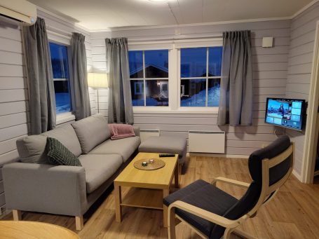 Ljust och modernt rum med soffa, bord och TV, fönster mot utsidan.