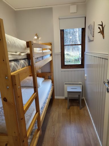 Sovrum med våningssäng, fönster och liten nattduksbord.